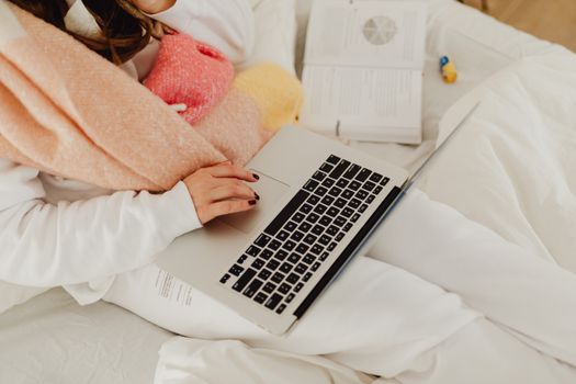 Woman in cozy setting using laptop in bed with open book and soft blanket.