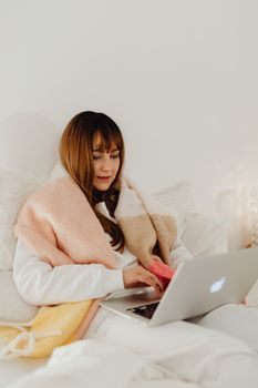 Woman comfortably using a laptop in bed with a cozy blanket, exuding warmth and relaxation.