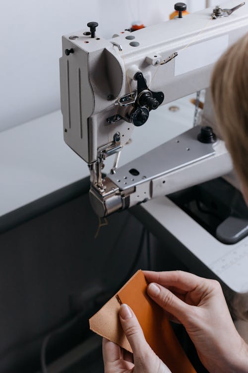Free Hands of a Woman Holding a Textile Near a Sewing Machine Stock Photo