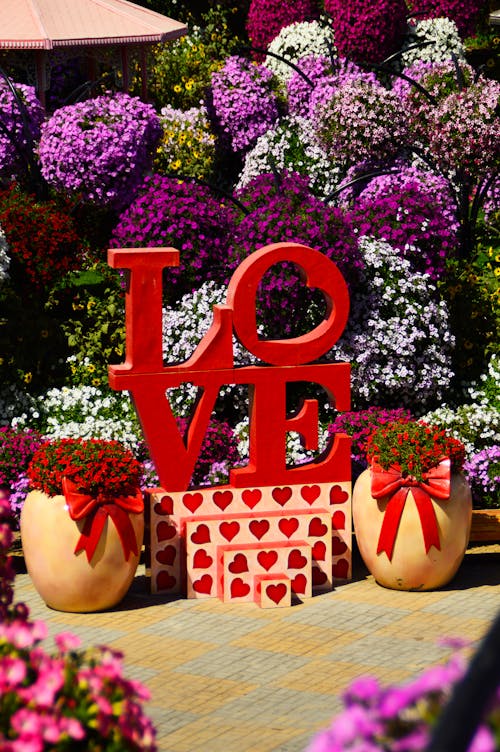 A Love Sculpture Between Potted Blooming Red Flowers in a Garden