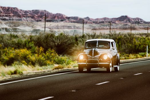 Vintage black car with headlights on driving through the scenic Arizona desert landscape.
