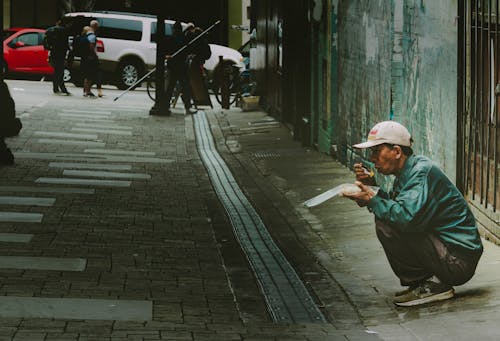 A Man Eating while Squatting on a Sidewalk