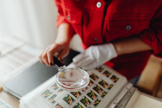 A person closely examines postage stamps with a magnifying glass, revealing intricate details.