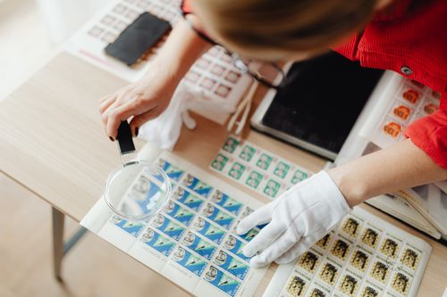 Free A person wearing white gloves inspects postage stamps using a magnifying glass. Stock Photo