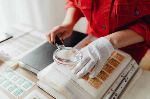 Free Close-up of a person examining stamps with a magnifying glass and gloves. Stock Photo