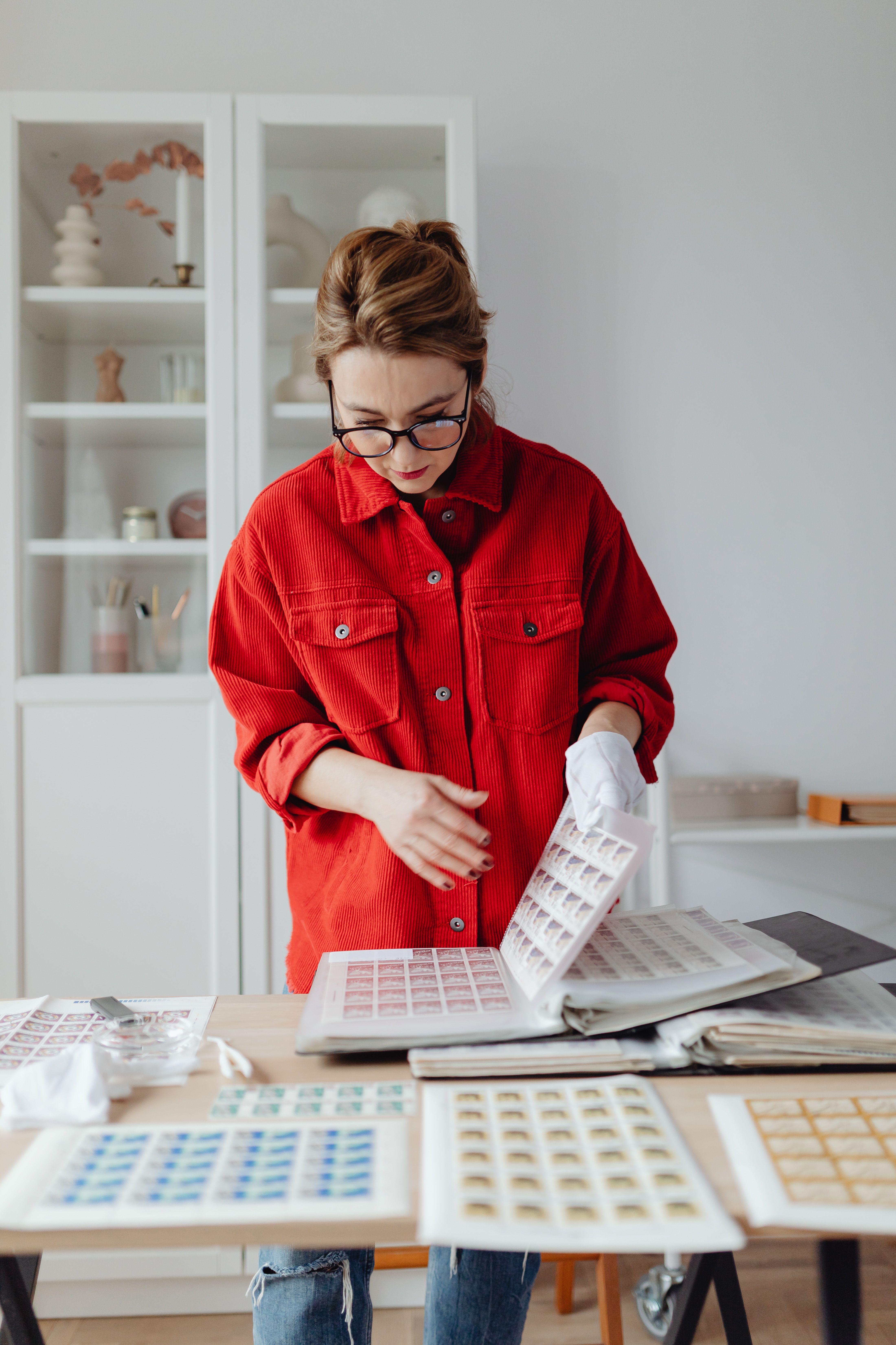 A woman in a red jacket examines a stamp collection indoors. Perfect for hobby and leisure themes.