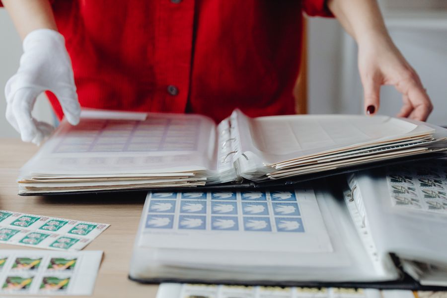 Person in red sorting a collection of vintage postage stamps using gloved hands on a wooden table.
