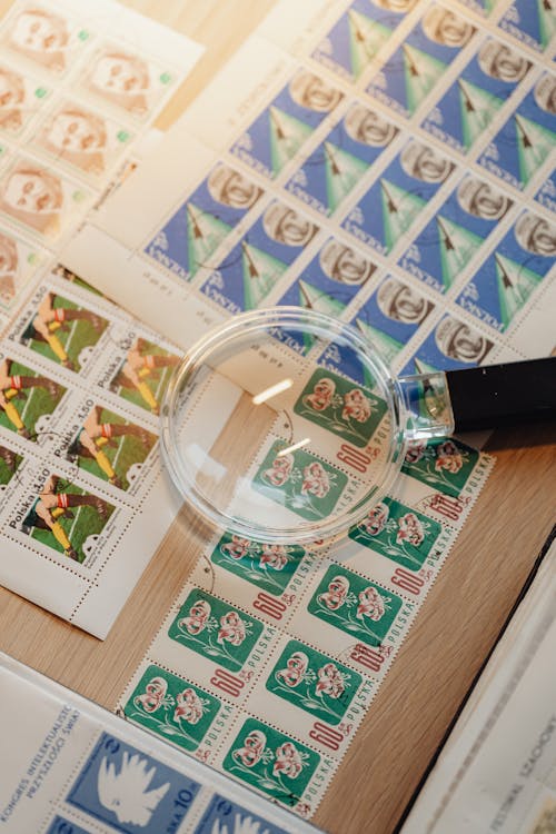 A Magnifying Glass on Postage Stamps on a Wooden Surface