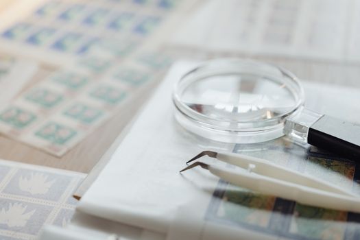 Magnifying glass and tweezers on a collection of postage stamps, ideal for philately enthusiasts.