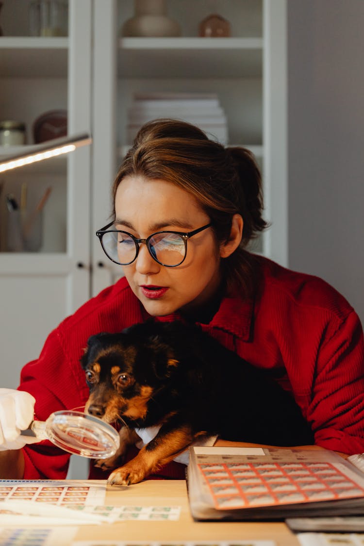 Woman Looking Through A Magnifying Glass With A Dog On Her Lap