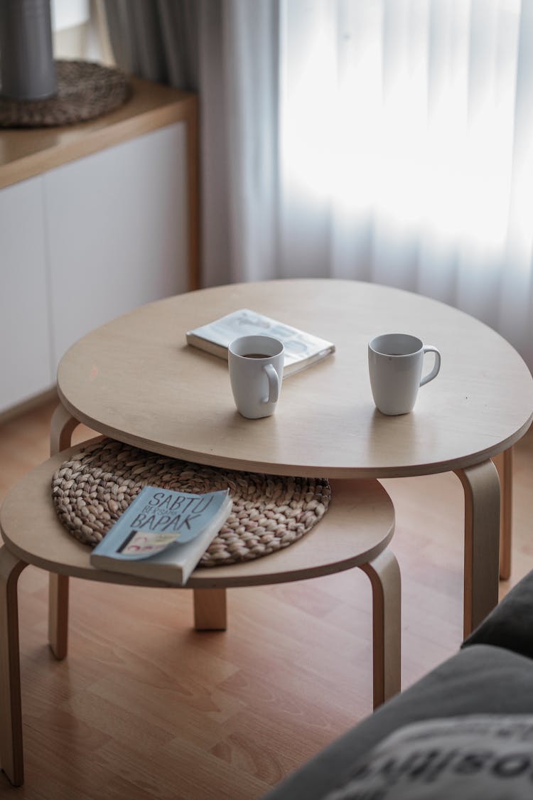 Two White Ceramic Mugs And Books On Round Wooden Tables