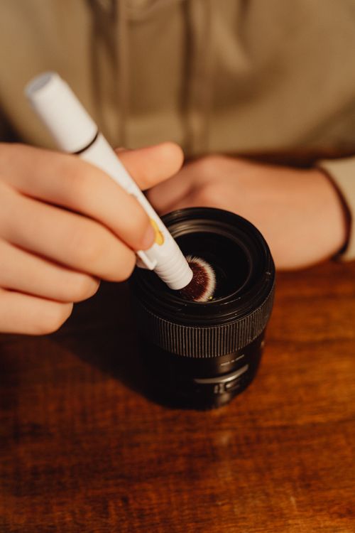 Free Close-up of a person using a brush to clean a camera lens, showcasing careful maintenance. Stock Photo
