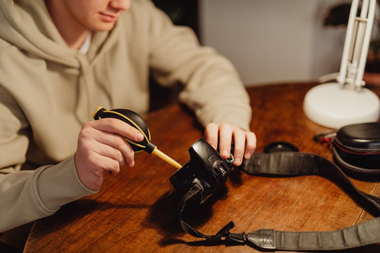 A Person Cleaning A Camera While Using A Bulb Blower