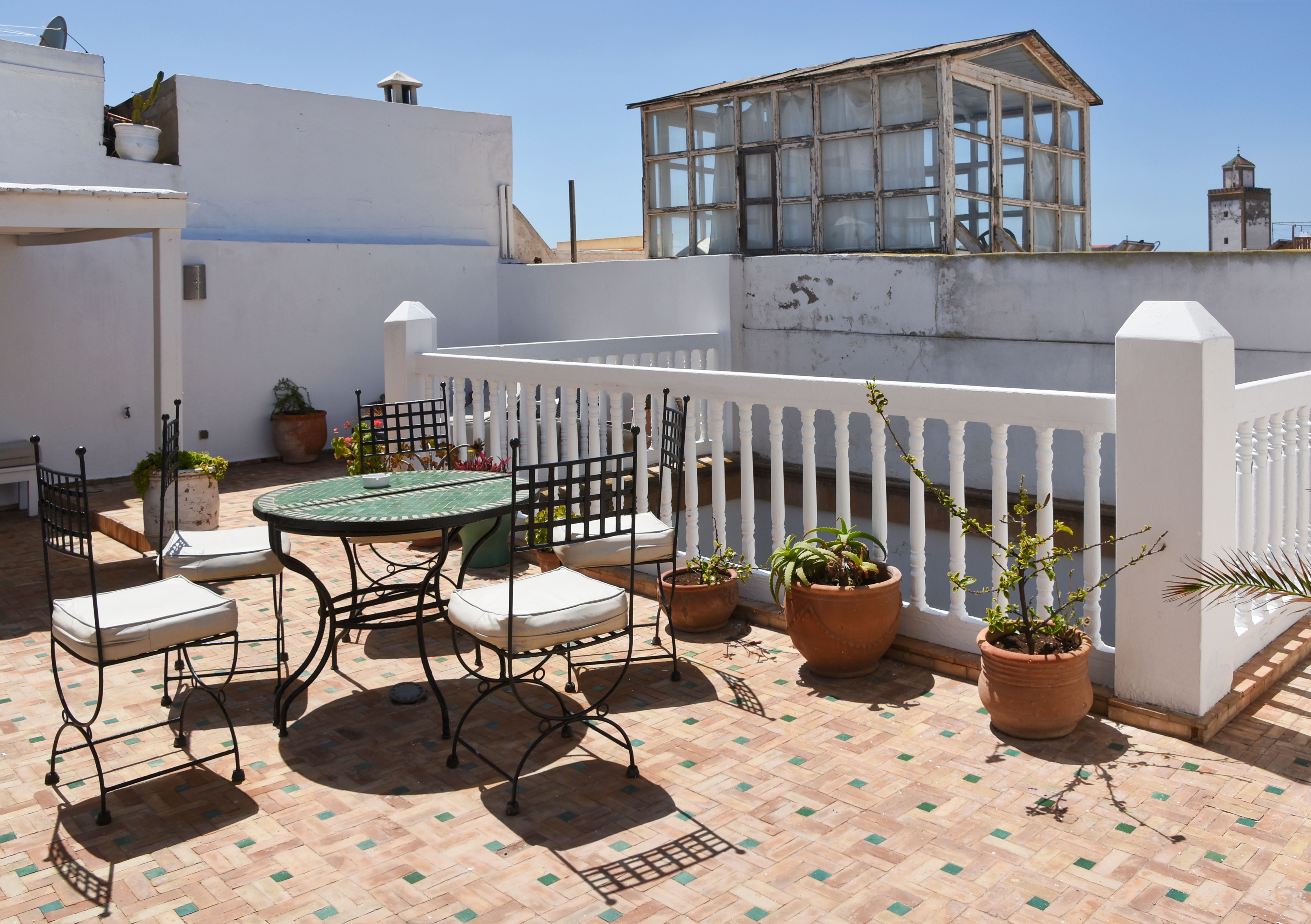 Sunny rooftop terrace in Essaouira, Morocco, featuring iron chairs, potted plants, and a tiled floor.
