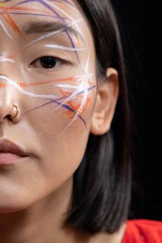 A close-up portrait of a woman with colorful face paint on a black background.