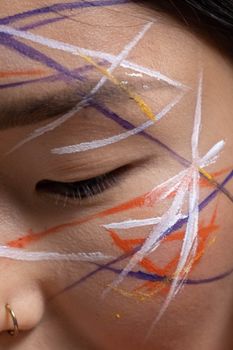 An artistic close-up of a woman's face with colorful abstract face paint and a nose ring.