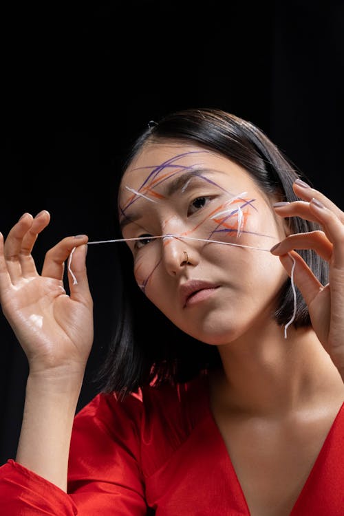 Woman in Red Shirt Applying Face Paint with a Thread