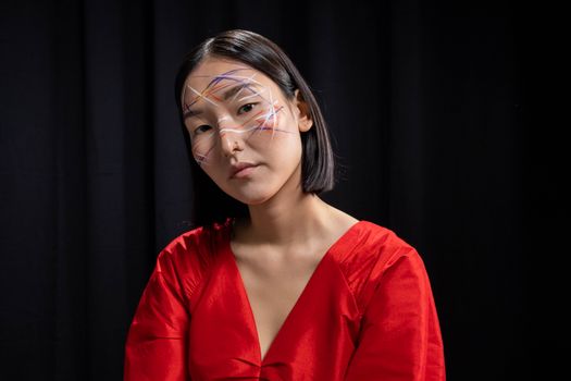 Close-up studio shot of a woman with artistic face paint and red dress against a dark background.