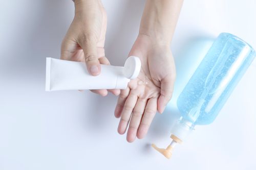 Free Hands using a white tube and blue bottle for skincare product application on a white background. Stock Photo