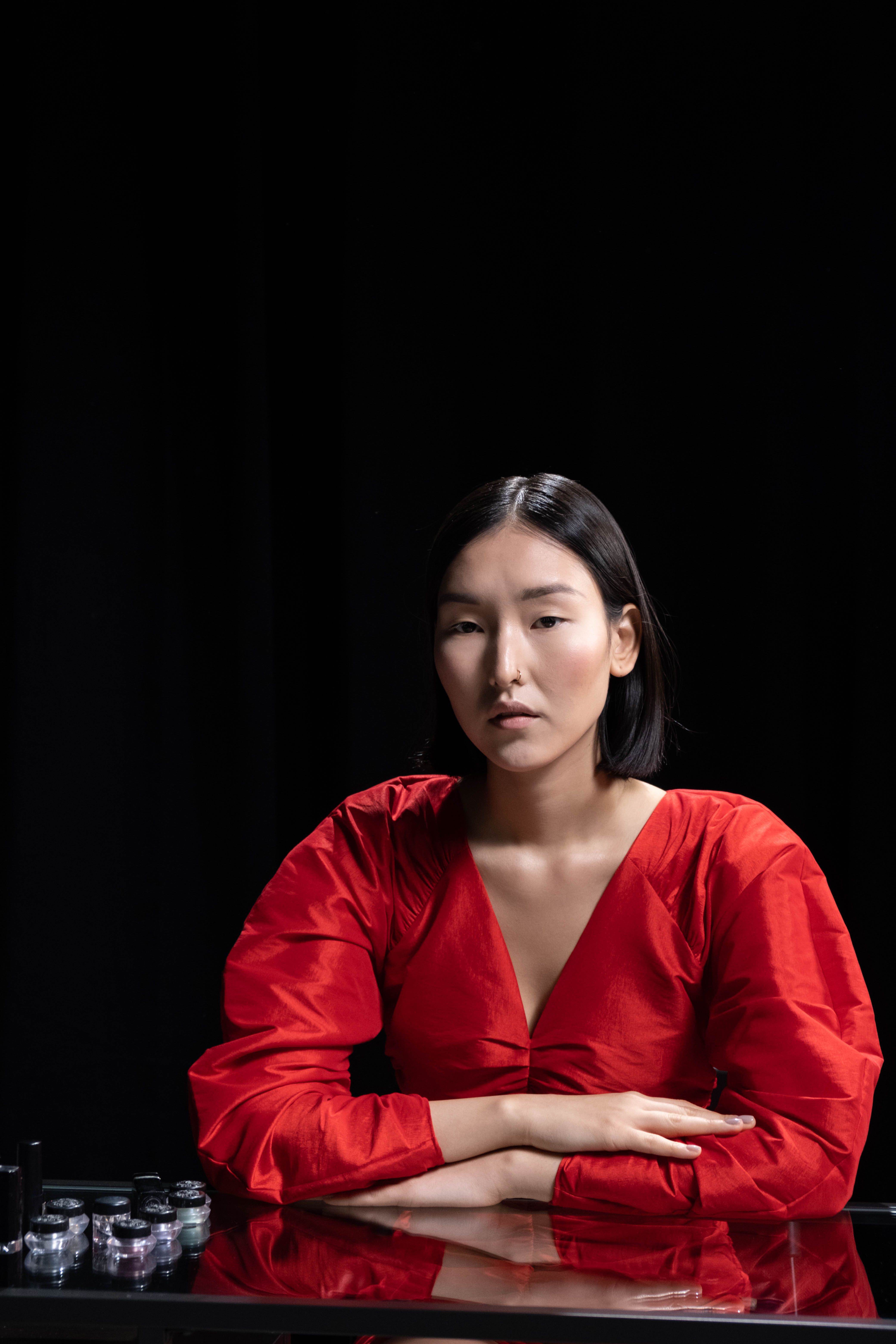 A serene portrait of a woman in a vibrant red dress against a black background, reflecting elegance.