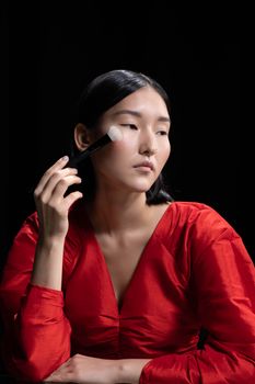 Portrait of a woman in a red dress applying blush on a black background.