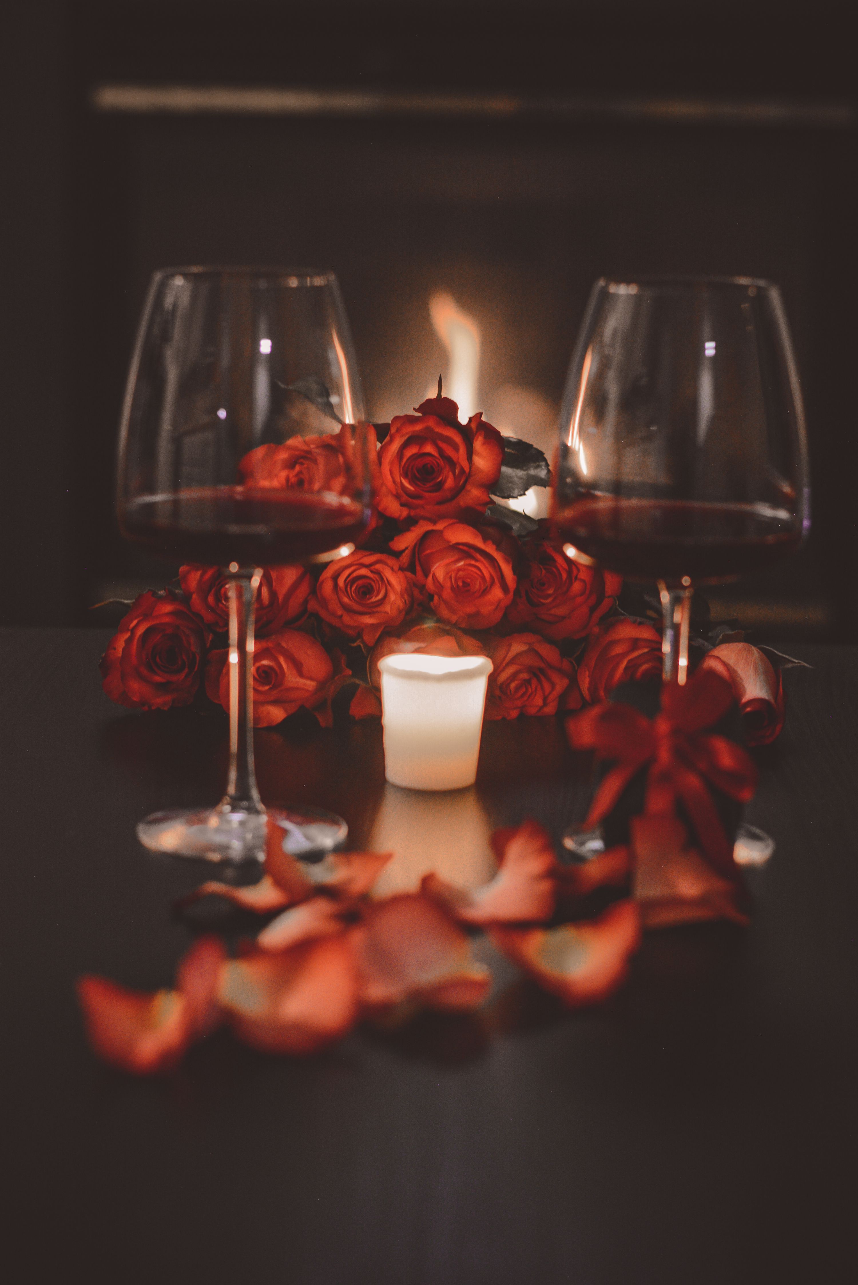 Elegant still life with red roses, wine glasses, and candles by a fireplace.