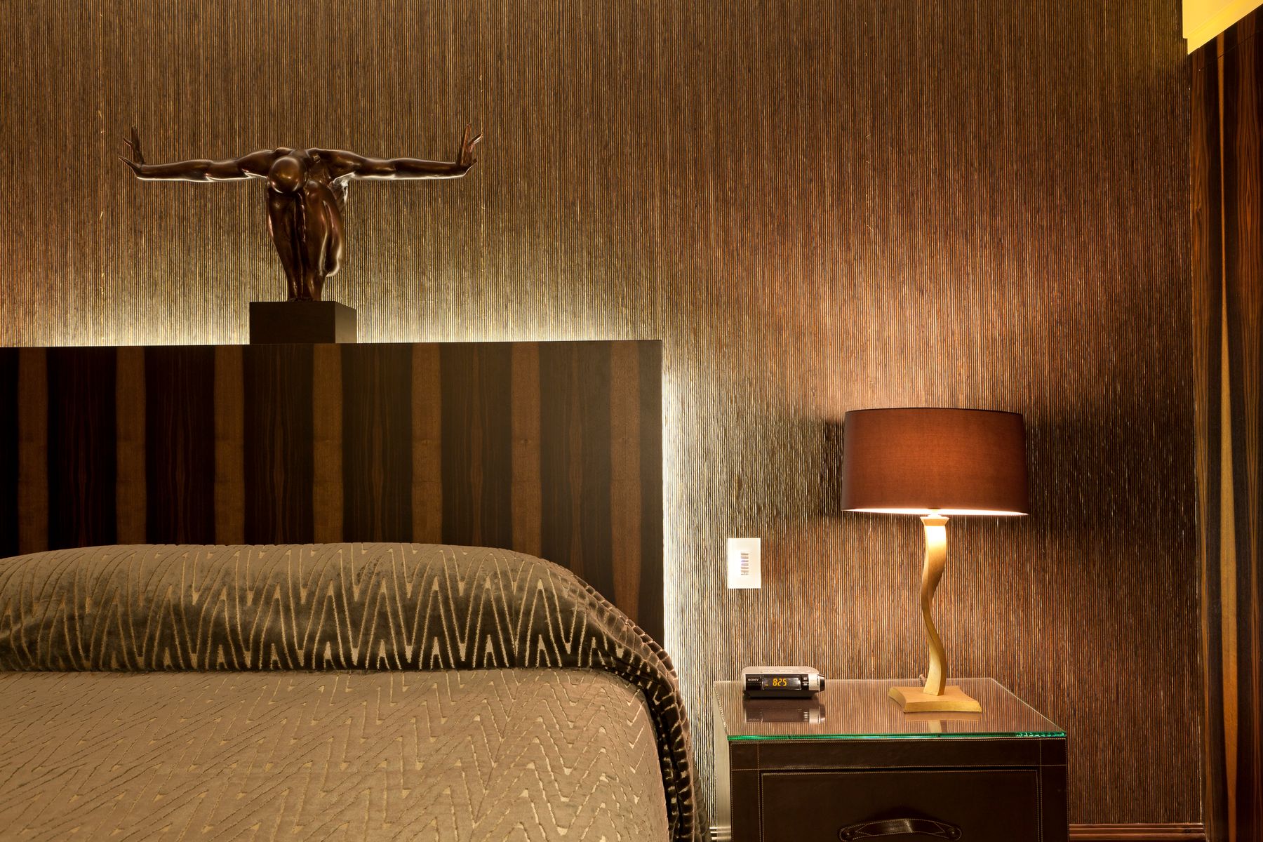 Warm bedside with a wood table, modern lamp, neutral bedding and small bronze sculpture