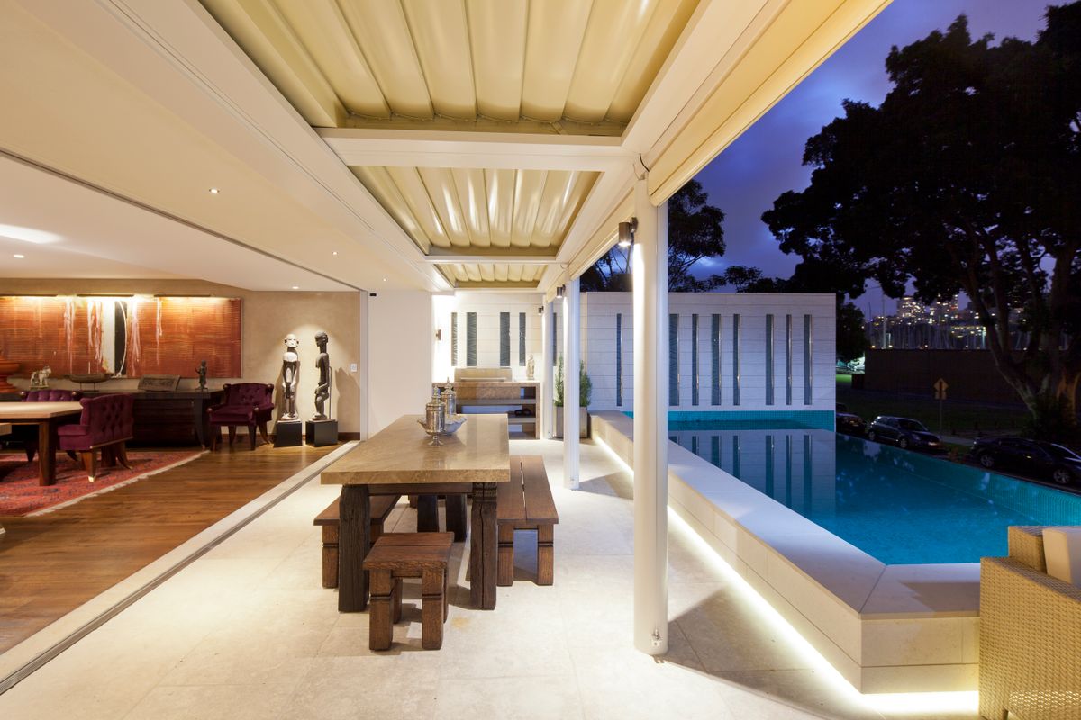 A covered terrace with a long table beside a pool at dusk