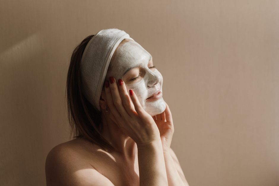 Woman with a facial mask and headband relaxing indoors, basking in soft sunlight. - Budget vs. Luxury: 5 Amazon Skincare Dupes That Work Just Like $100 Creams