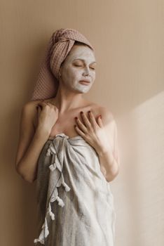 Woman enjoying a skincare facial mask, wrapped in a towel indoors, epitomizing self-care and relaxation.