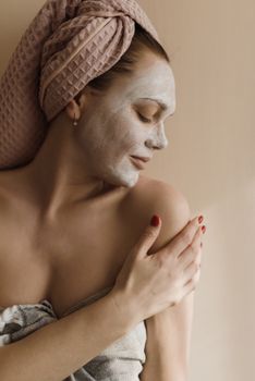 Serene woman with a facial mask enjoying a skincare routine, wrapped in a towel.