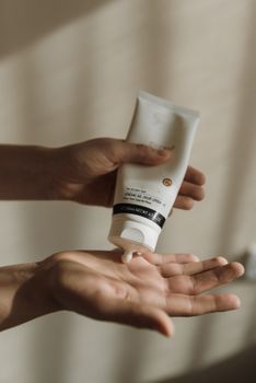 Hand squeezing skincare cream from a tube, captured in a gentle indoor setting.