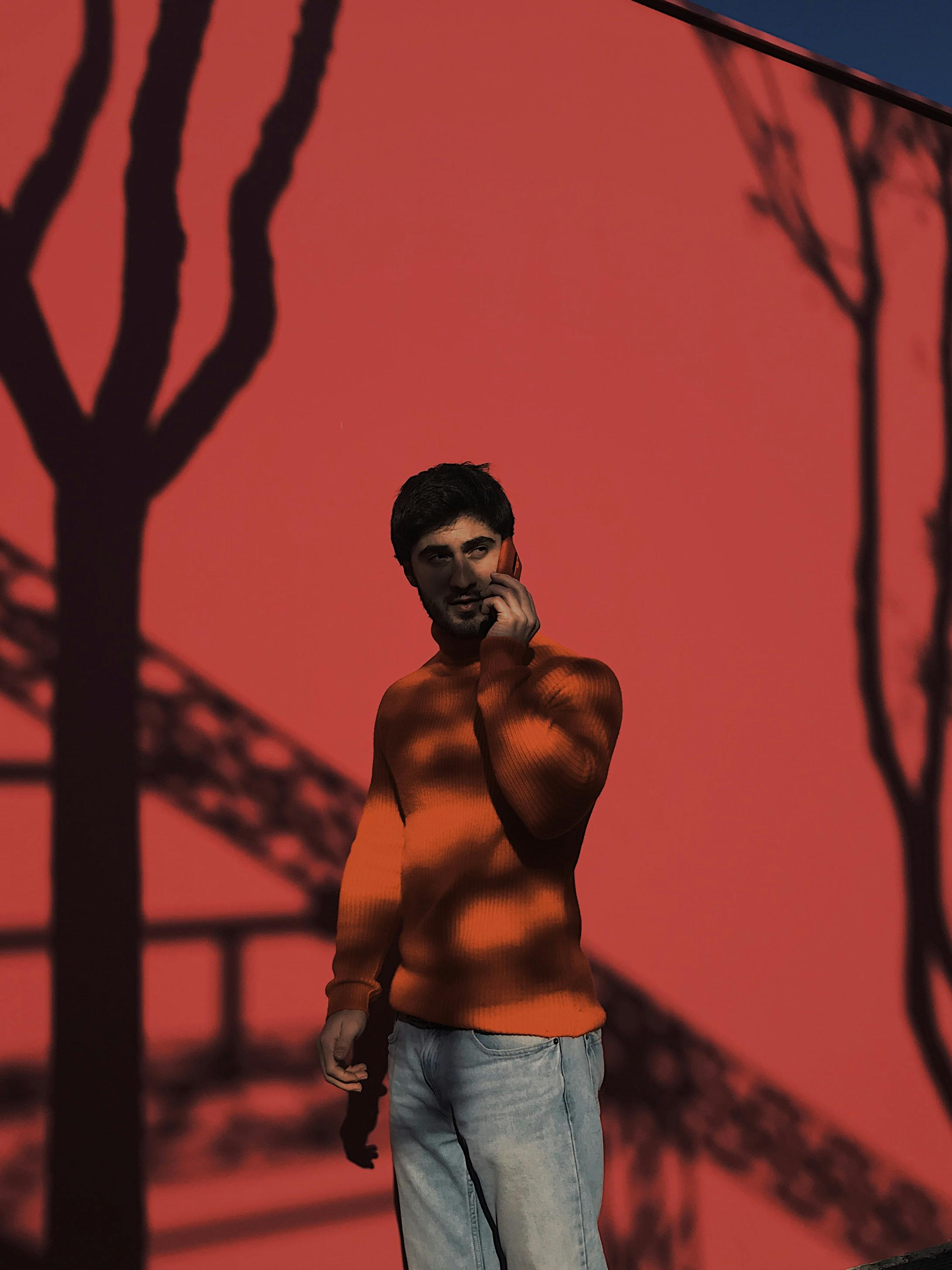 Serious ethnic male standing near vivid wall with shadows and having conversation on mobile phone while looking away