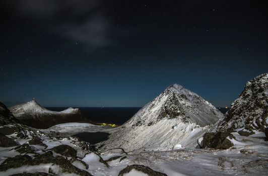 A breathtaking view of a snowy mountain range under a star-filled night sky in Myrland, Norway.