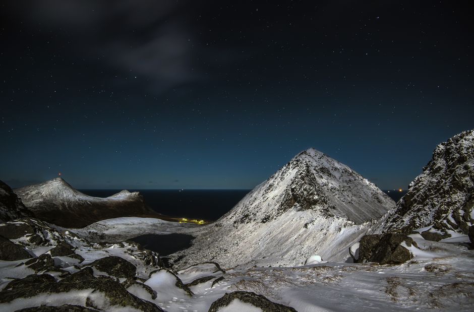 A breathtaking view of a snowy mountain range under a star-filled night sky in Myrland, Norway.