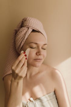 A woman enjoys a relaxing facial treatment using a gua sha tool for skincare at home.