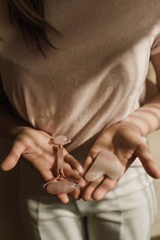 Person holding a jade roller and heart-shaped gua sha tool in hands for skincare treatment.