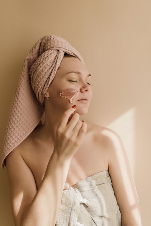 Free Woman enjoying a calming skincare routine with a facial roller indoors. Stock Photo
