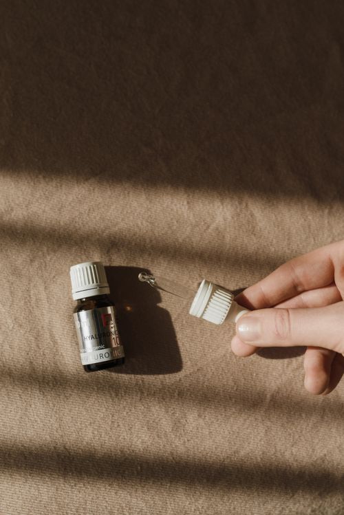 Free Minimalist skincare dropper in hand casting a shadow on brown fabric, perfect for beauty concepts. Stock Photo