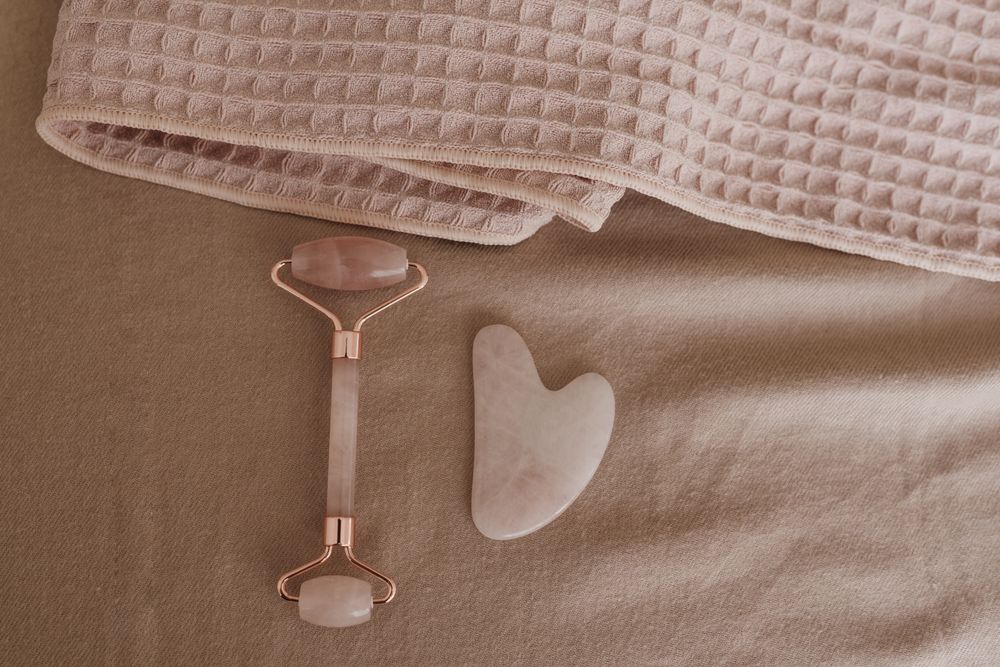 A rose quartz facial roller and gua sha stone resting on a soft pink towel