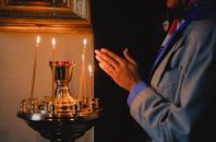A person praying beside lit candles in a religious setting, evoking peace and spirituality.