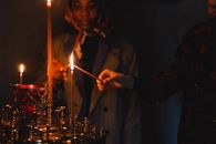 Two individuals participating in a candle lighting ritual in a dark room, creating a warm and serene atmosphere.