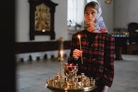 Woman in Red Black and White Plaid Scarf Standing in Front of Lighted Candles