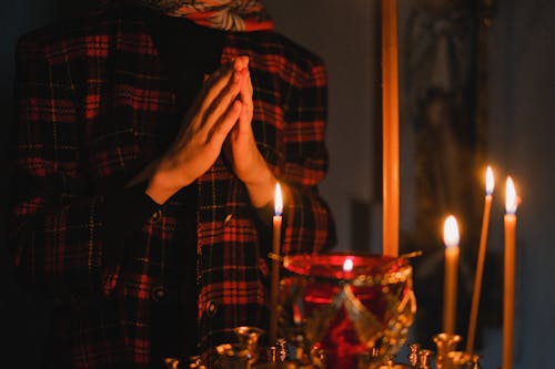 Free Person in Red and Black Plaid Long Sleeve Shirt Praying Before Lighted Candles Stock Photo