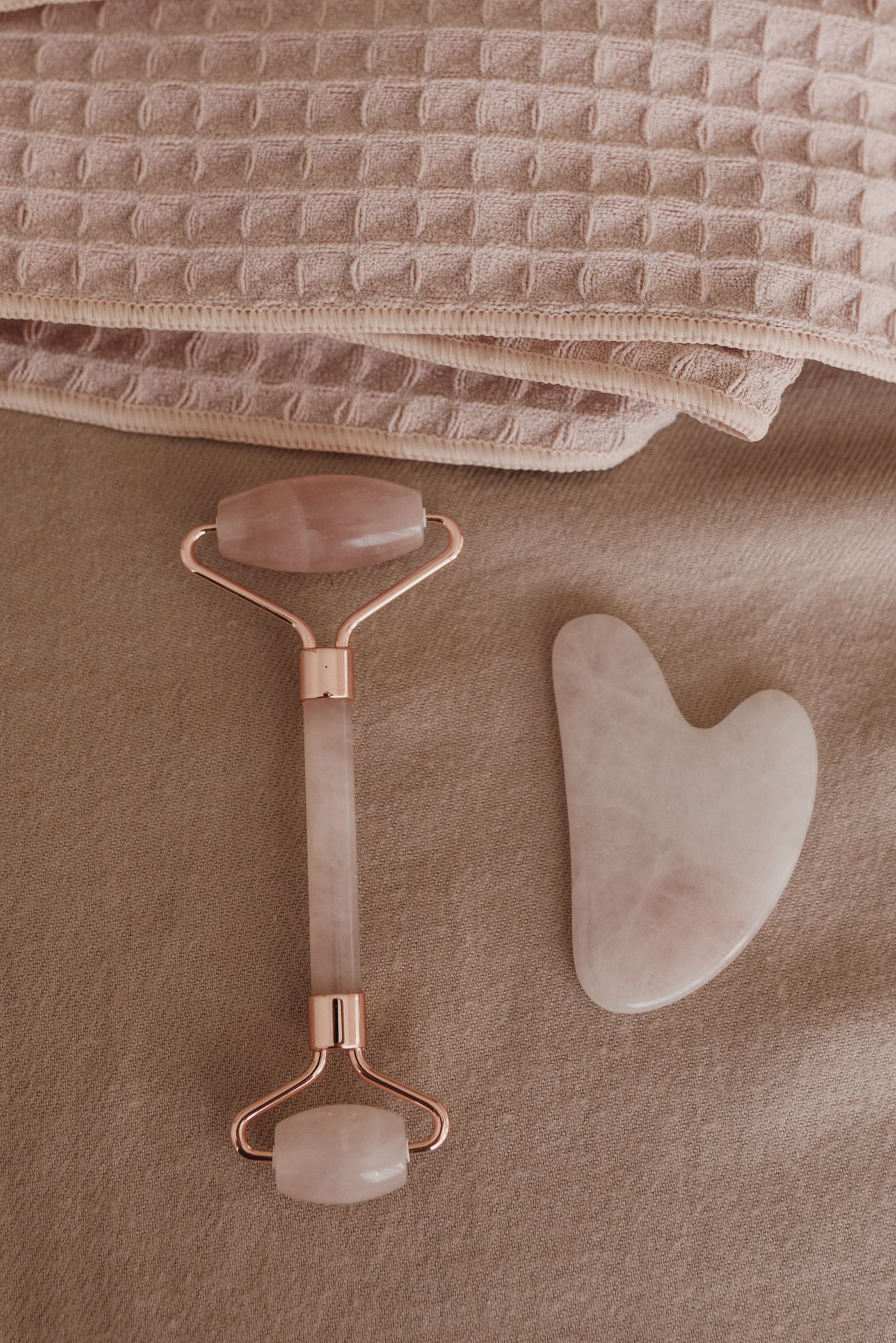 Rose quartz facial roller and gua sha skincare tools arranged on soft neutral fabric