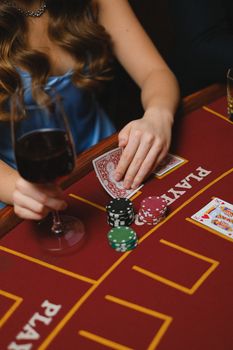 A woman holding cards and a wine glass at a casino, playing poker.