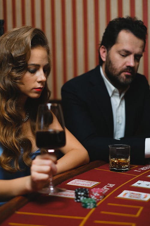 Man in Black Suit Jacket Playing Poker Beside a Woman in a Casino