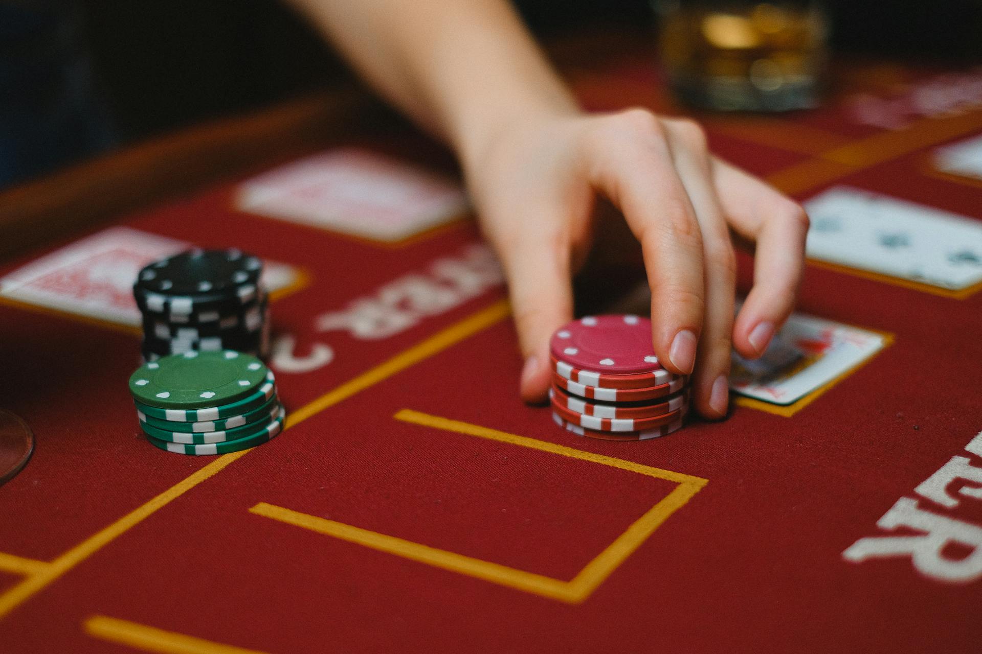 Hand handling poker chips on a casino table with cards, highlighting gambling activity.