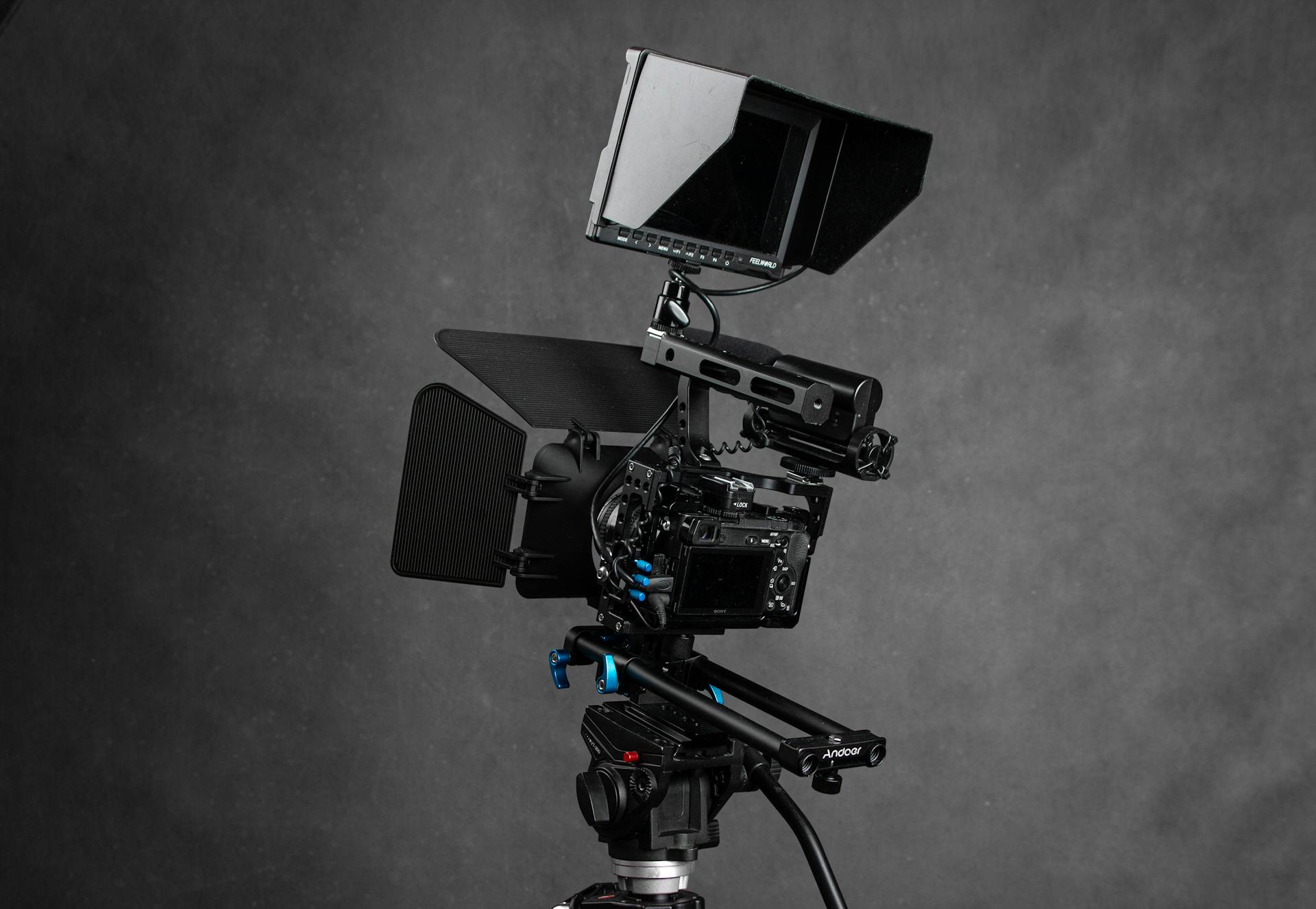 Modern black video camera with black screen on monitor and wires placed on gray background in professional studio with equipment