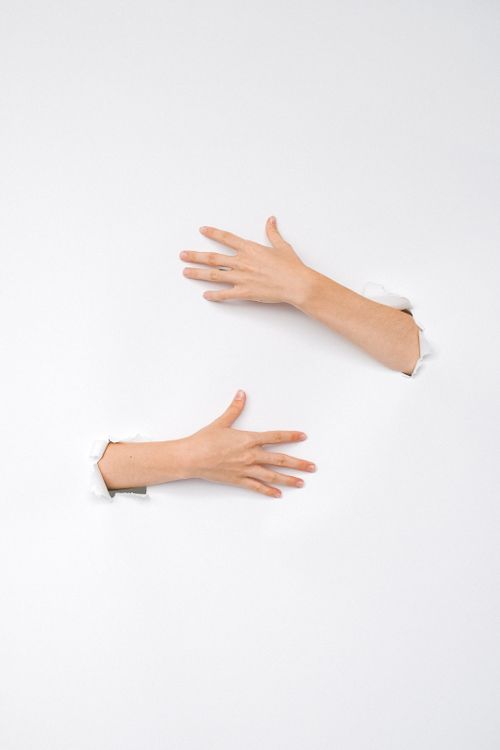 Free Two human hands reaching through holes in a white wall, symbolic of connection and exploration. Stock Photo